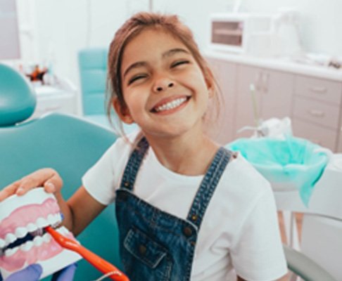 Child smiling next to model of teeth with toothbrush