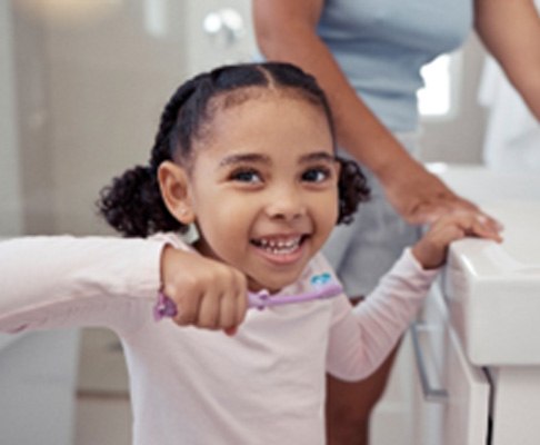 Young girl smiling while brushing her teeth