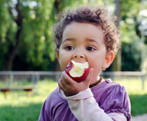 : Closeup of child biting into red apple outside