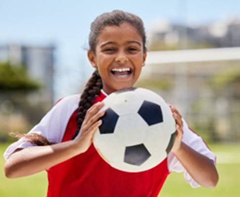 Teen girl smiling while holding soccer ball on the field