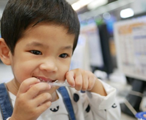Closeup of young boy using teeth to open package