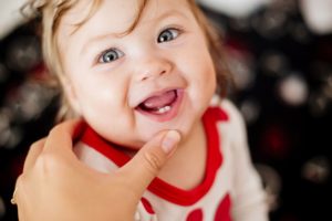 Infant in a white and red shirt with 2 bottom teeth grown in