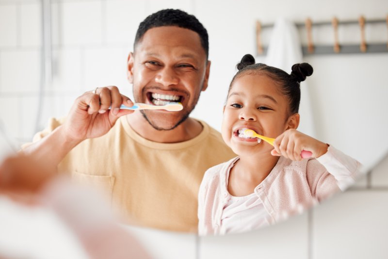 Dad and daughter brushing together for good oral hygiene