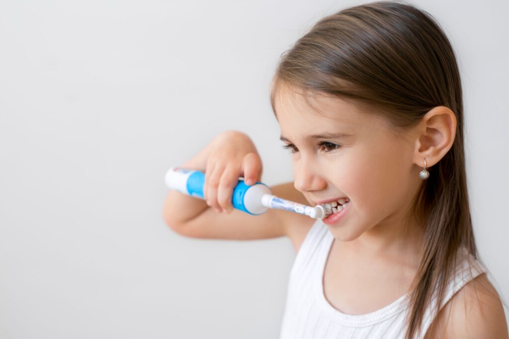 Girl with brown hair brushing teeth with electric brush