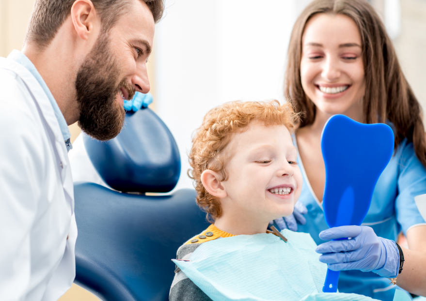 Boy in dental chair looking at mirror while dental team smiles