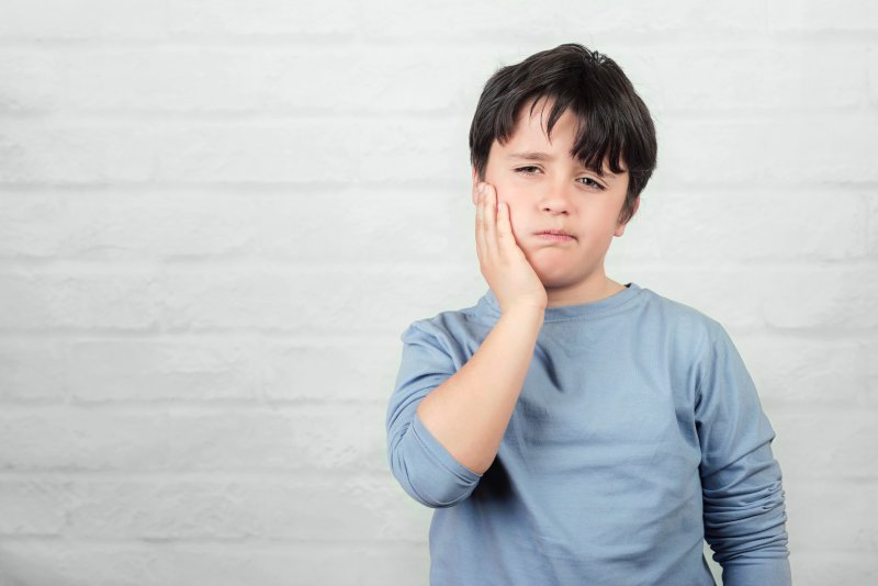 a boy holding his cheek due to a sensitive tooth