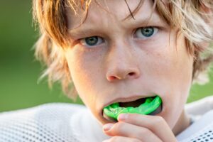 Boy inserting green mouthguard over upper arch